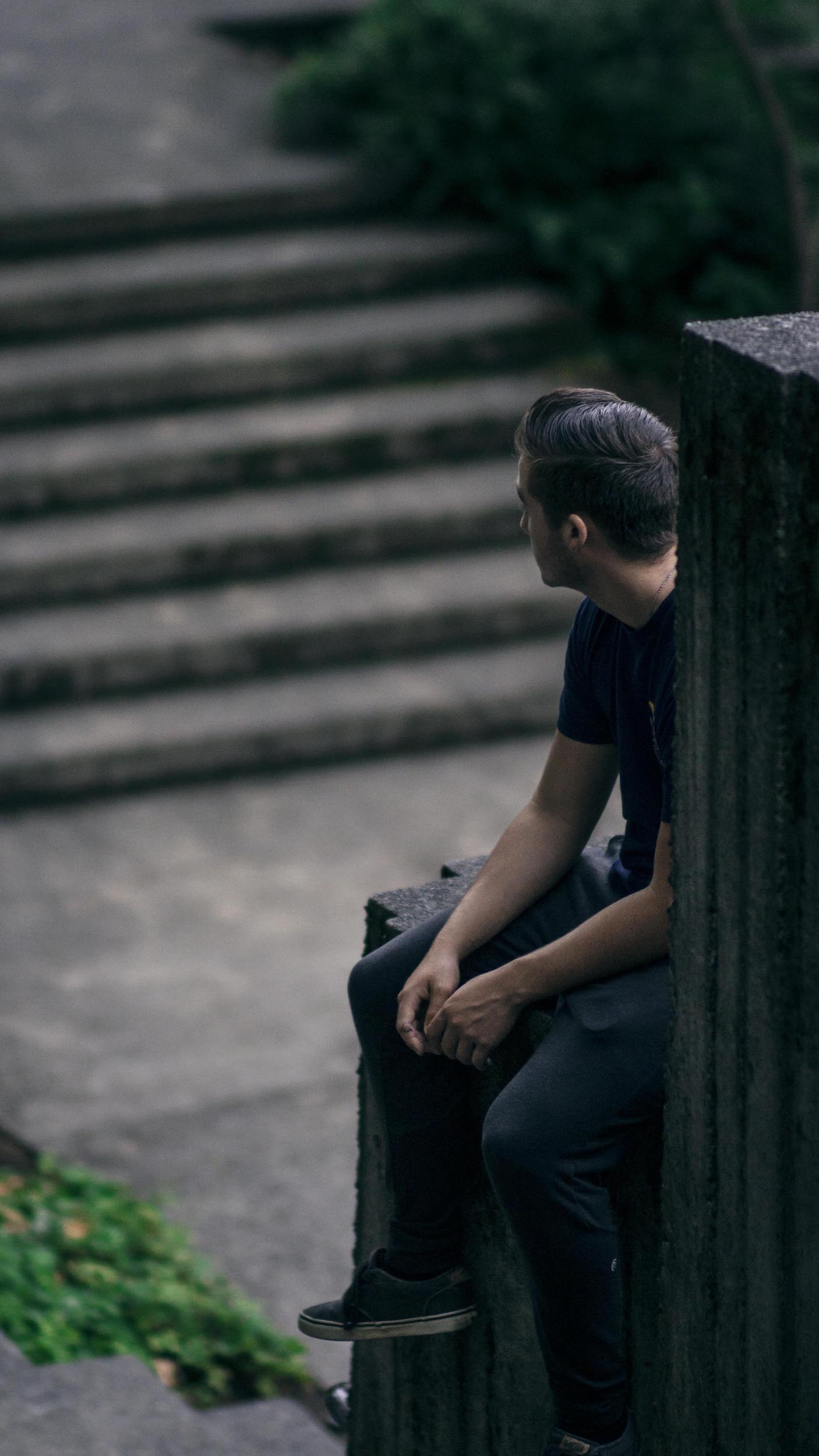 male figure sitting atop concrete structure, looking out of frame