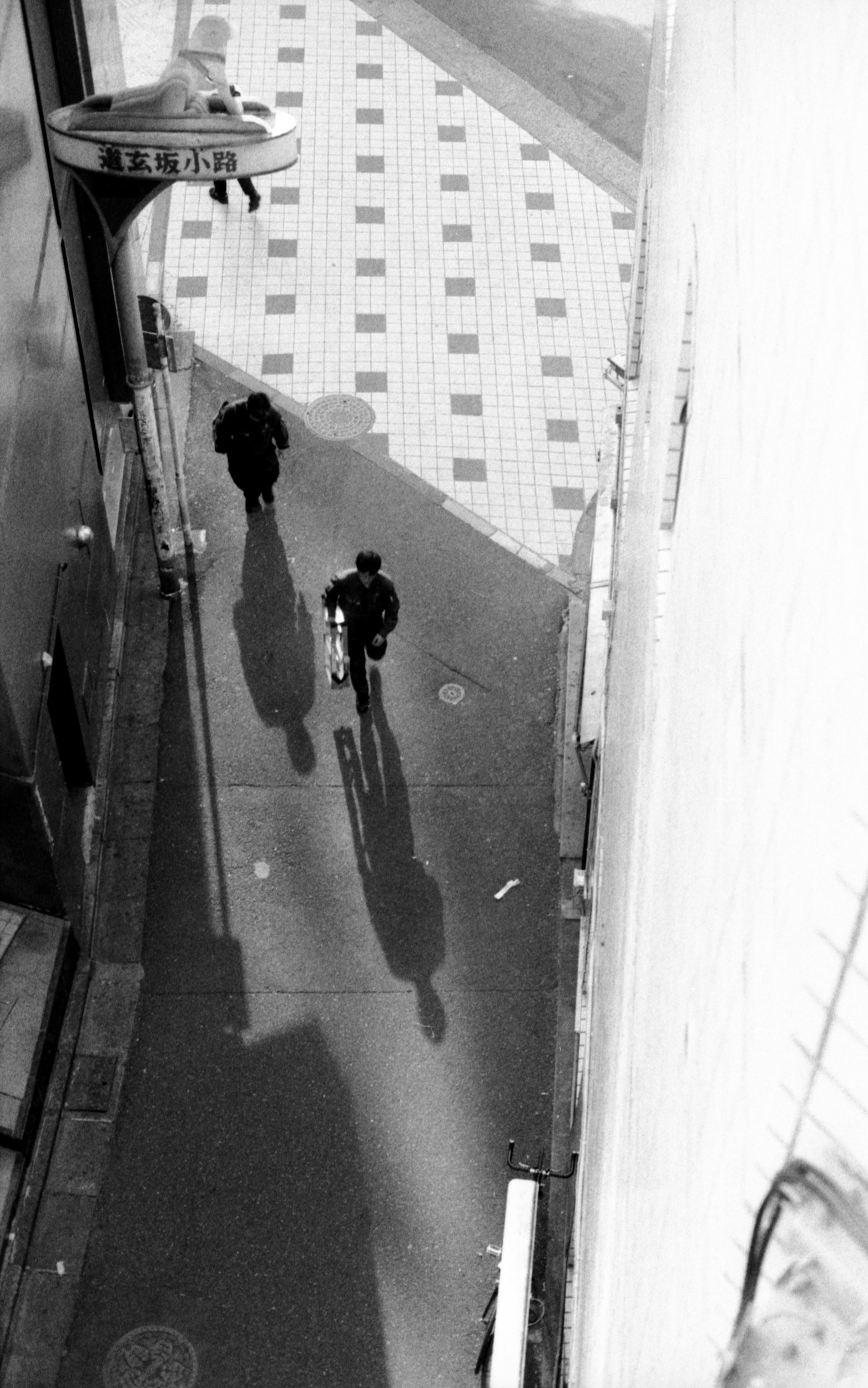 two men casting long shadows down an alley in japan, 35mm black and white film