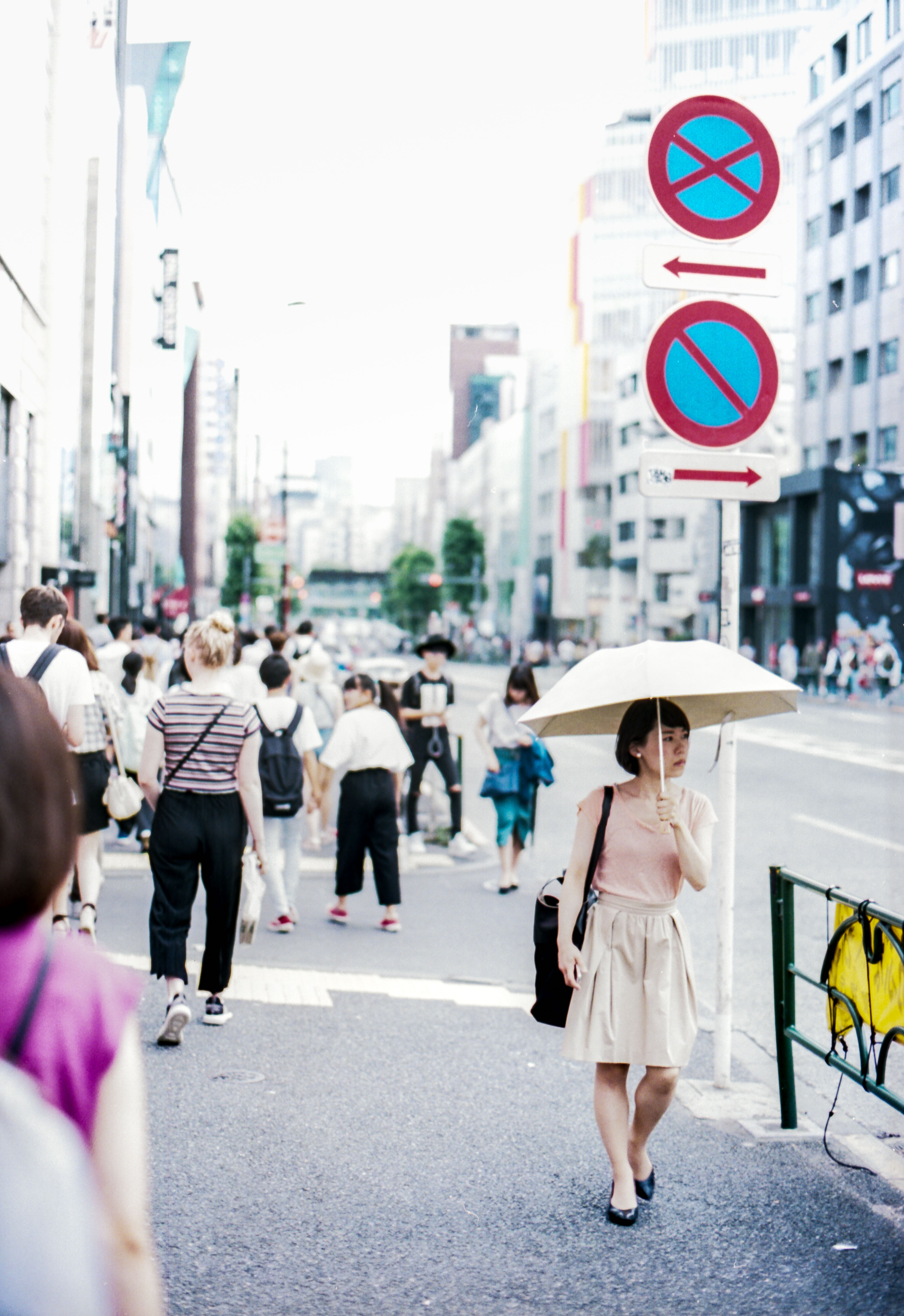 woman with parasol walks beneath street sign and looks to her side, in away from sidewalk crowd, japan, 35mm film