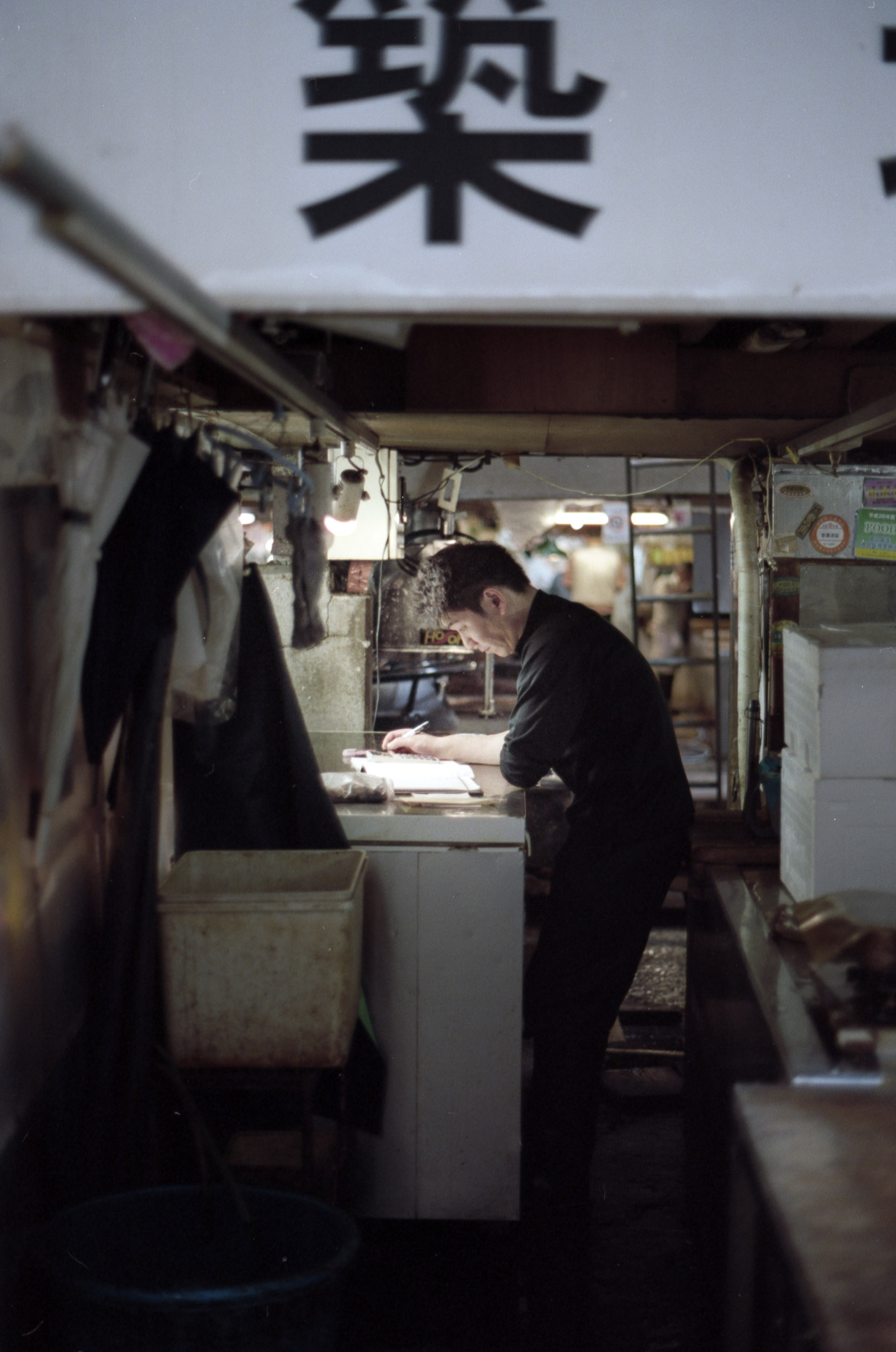 man leans over paperwork at tsukiji fish market, japan, 35mm film
