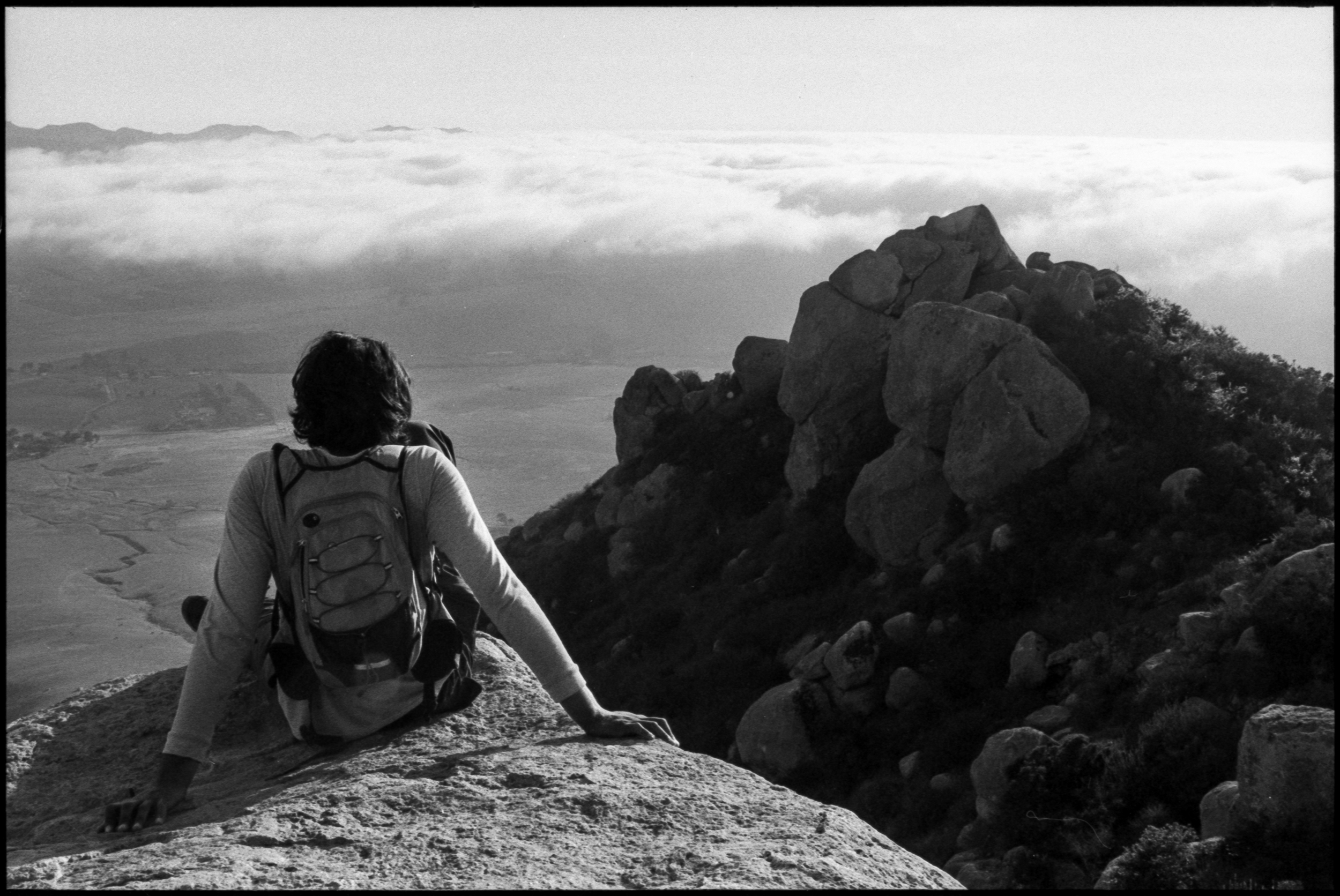 person sitting on a boulder overlooking a foggy landscape, 35mm film