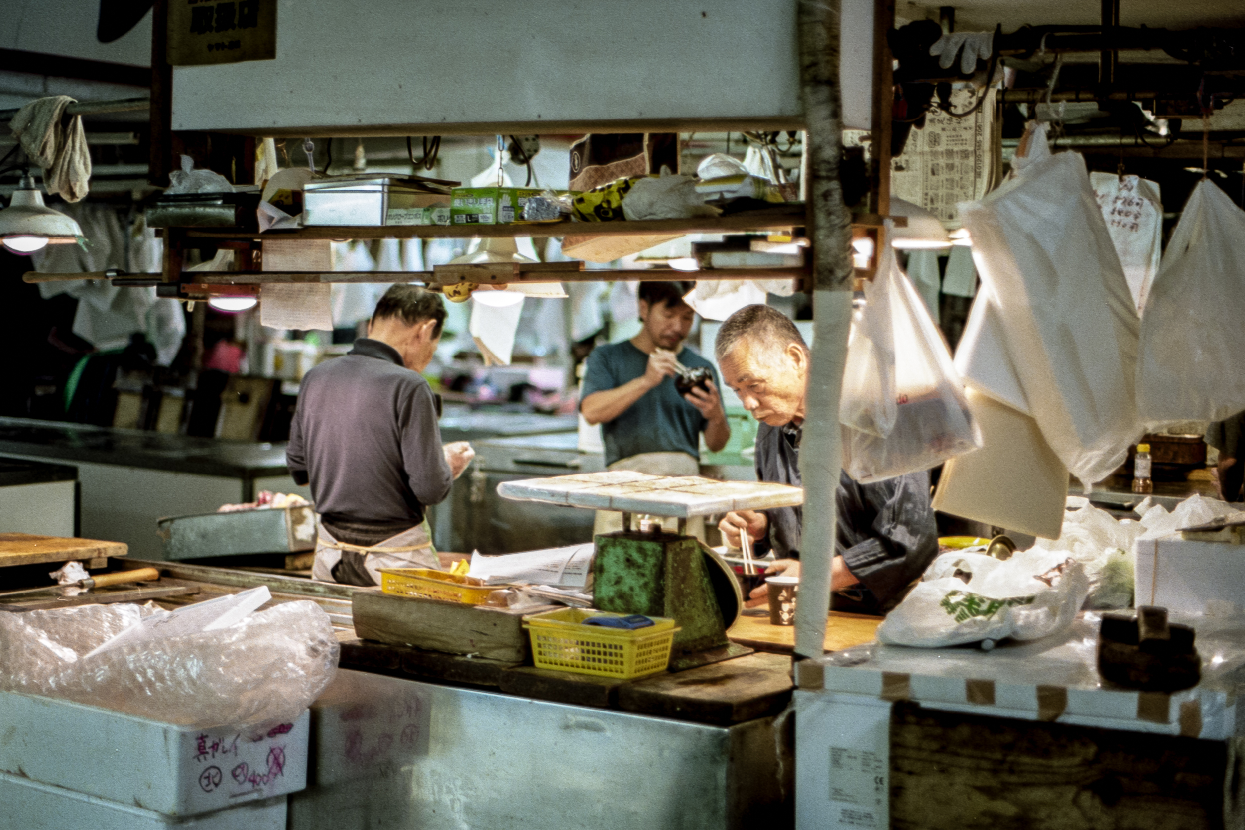 a group of men eating breakfast among their workstation at tsukiji fish market in japan, 35mm film