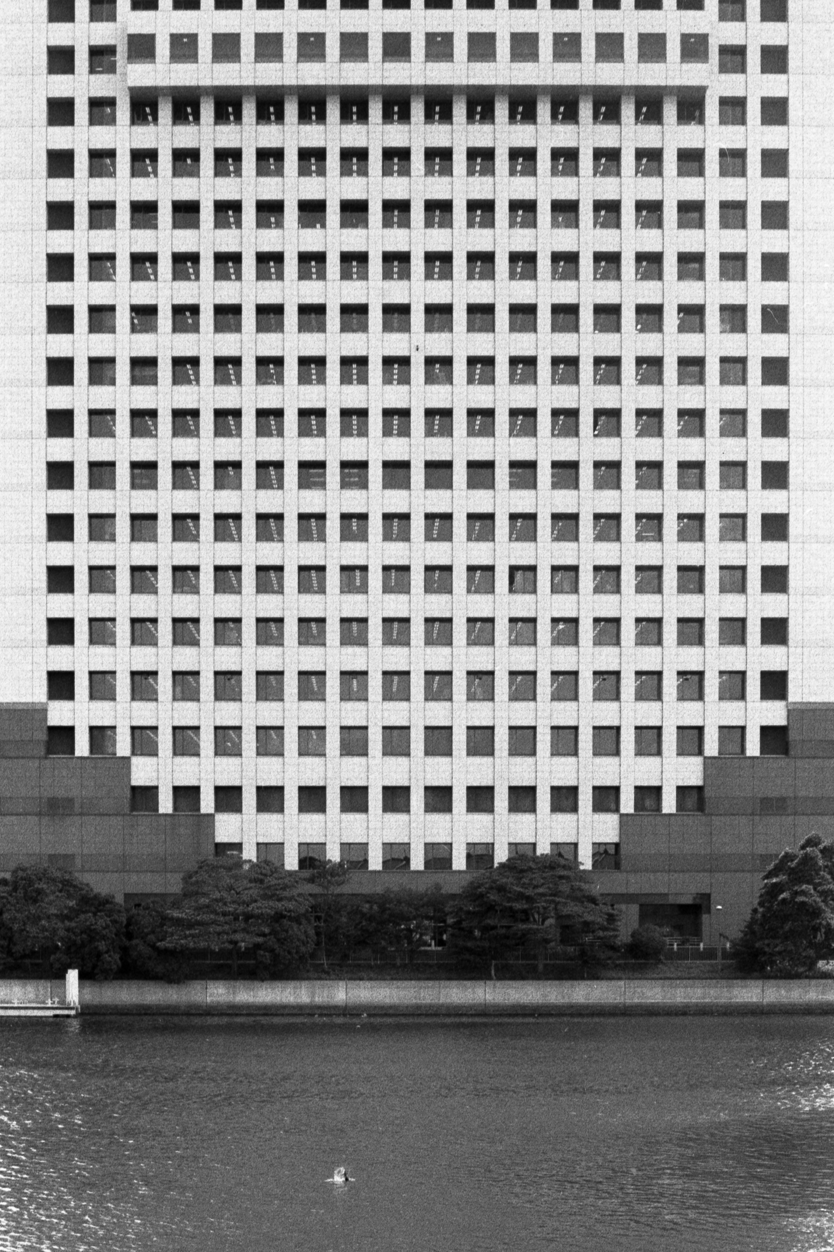 exterior building with perfect grid of square windows with river in foreground, 35mm black and white film