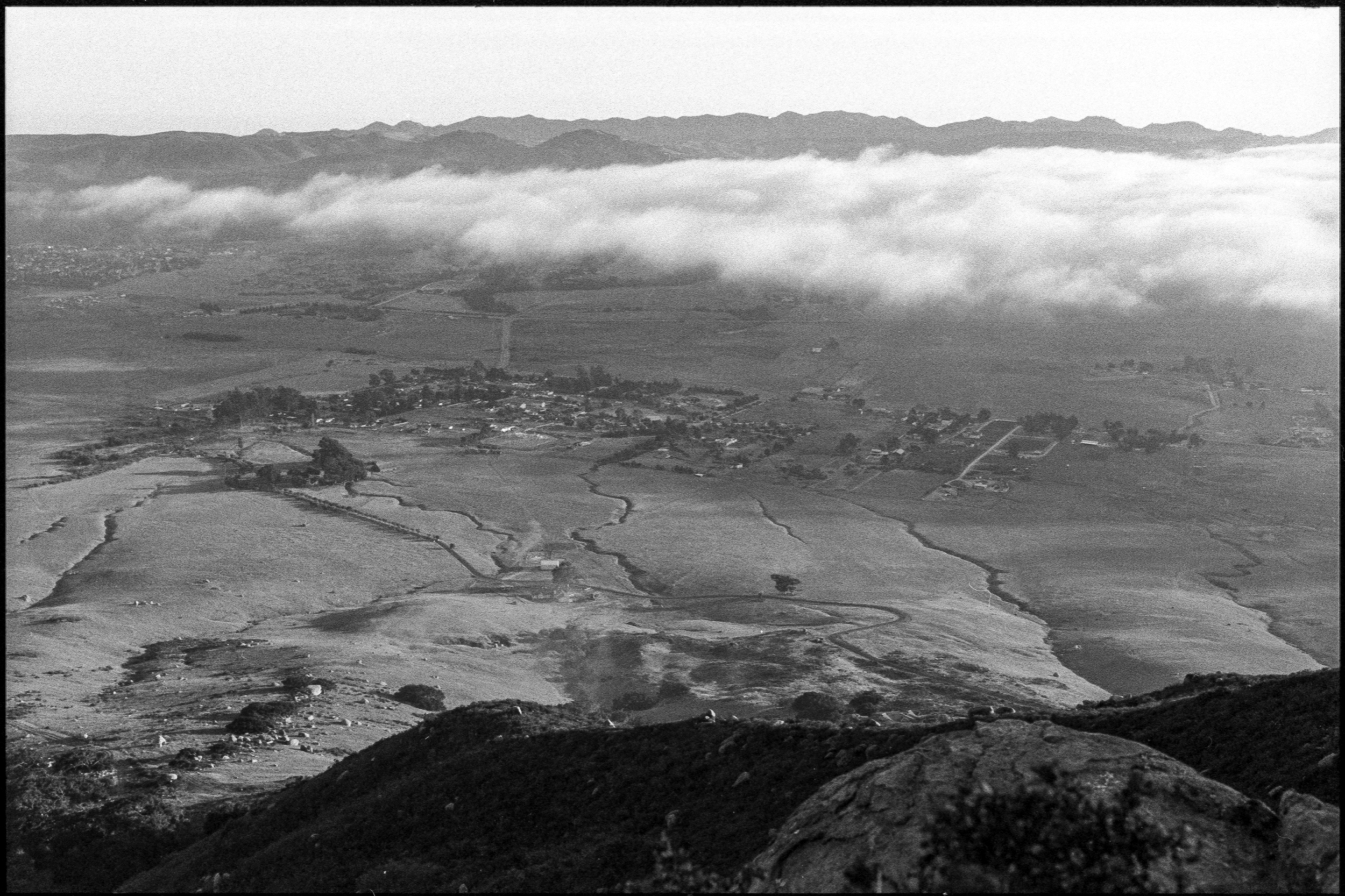 a thin layer of marine clouds drifts above a small cluster of buildings in a valley, 35mm film