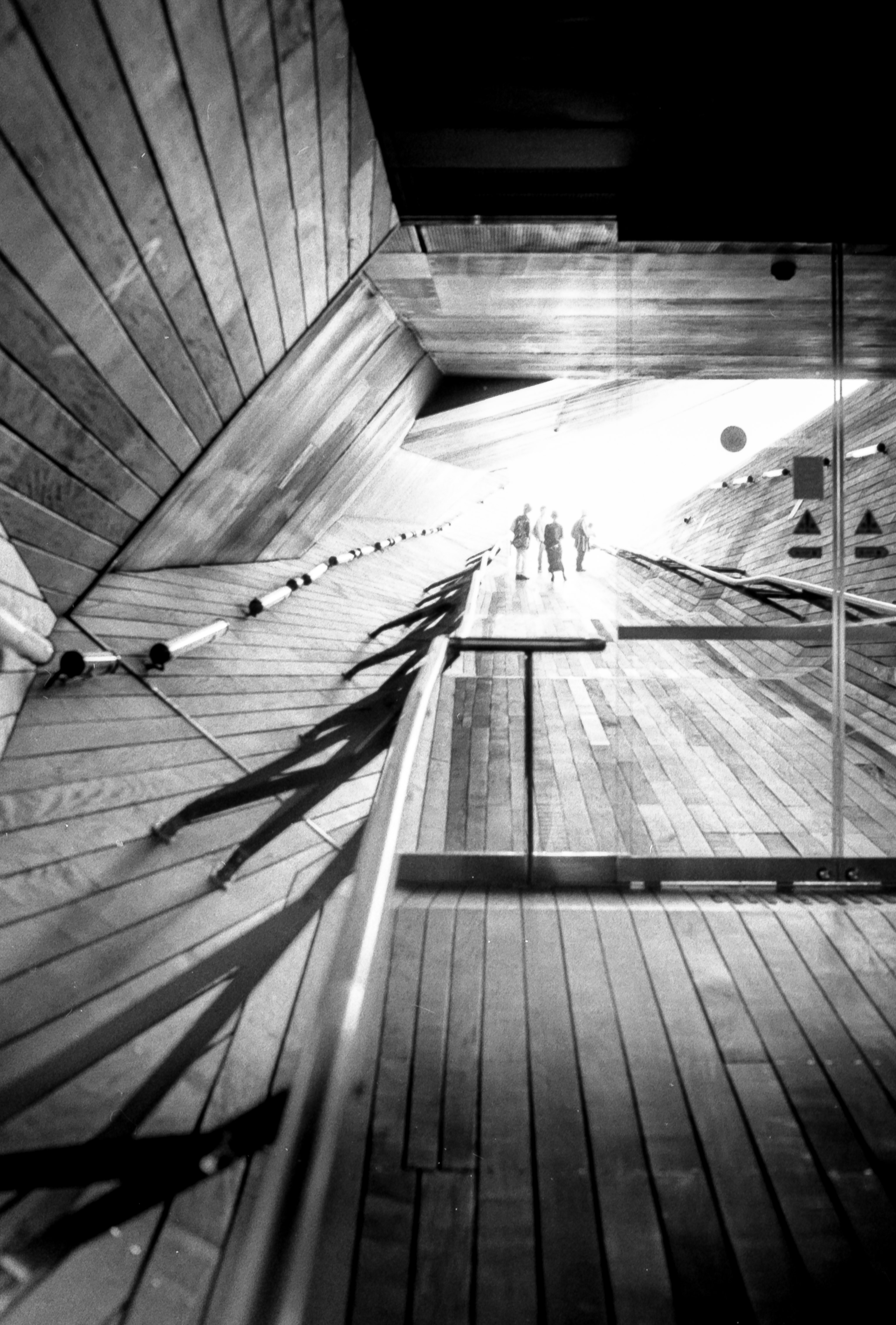interior of yokohama port terminal wooden walkway with glass door, silhouetted figures in background, 35mm black and white film