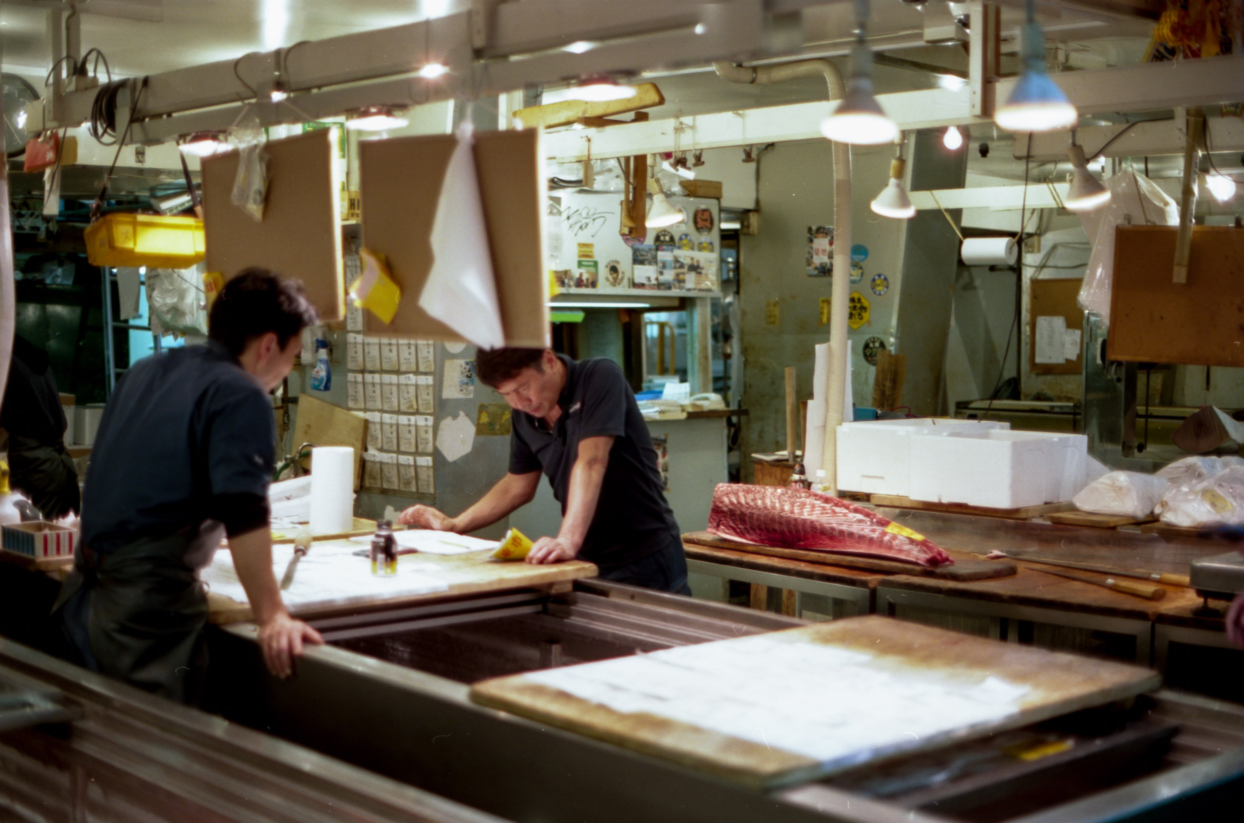 large tuna carcass waiting to be carved while men check paperwork in tsukiji fish market japan, 35mm film