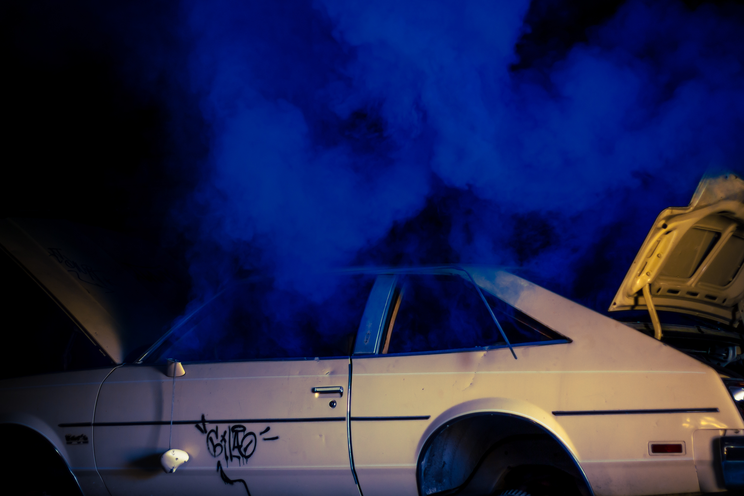 a dilapidated old car in a dark garage with blue smoke floating out of its windows
