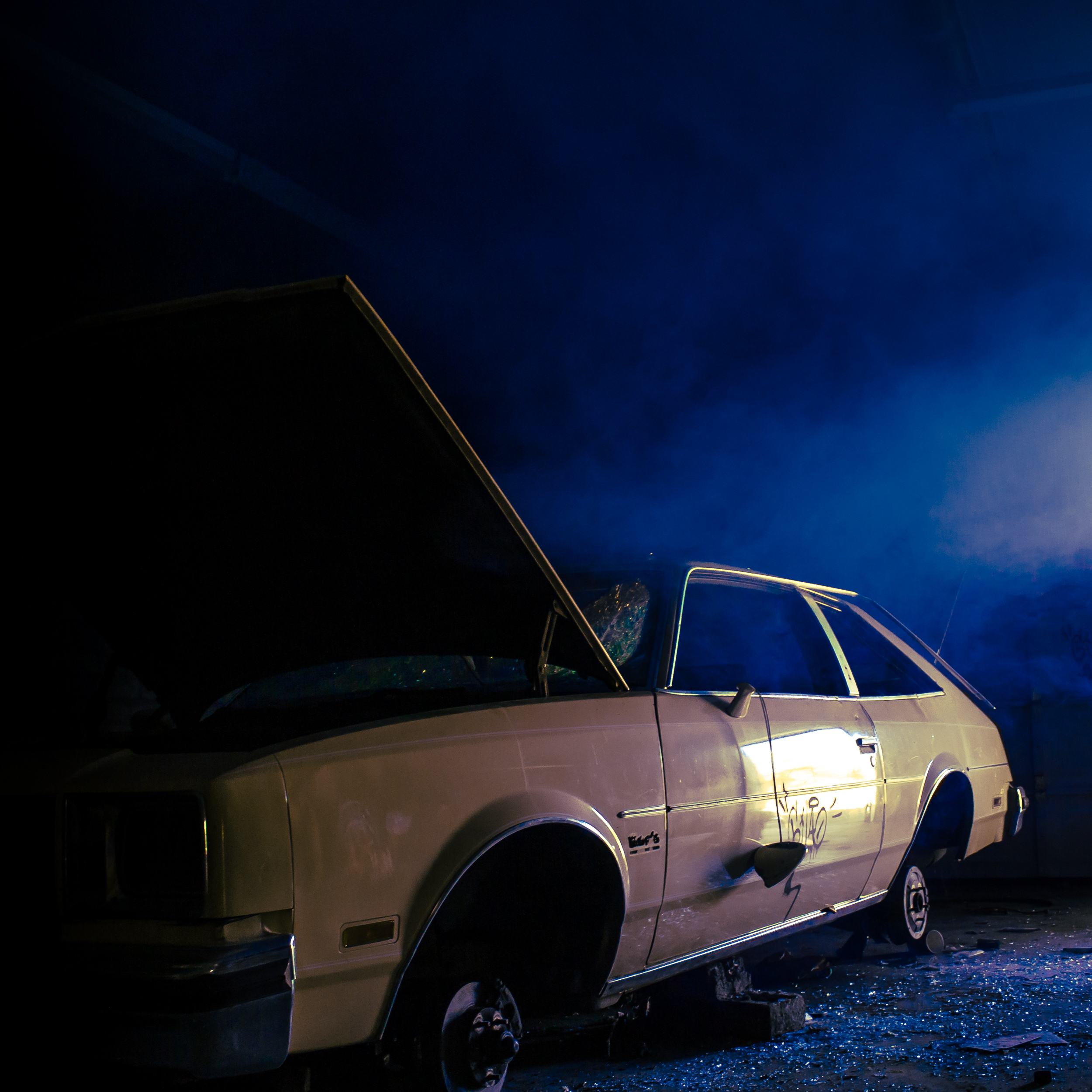 a dilapidated old car in a dark garage with blue haze floating above