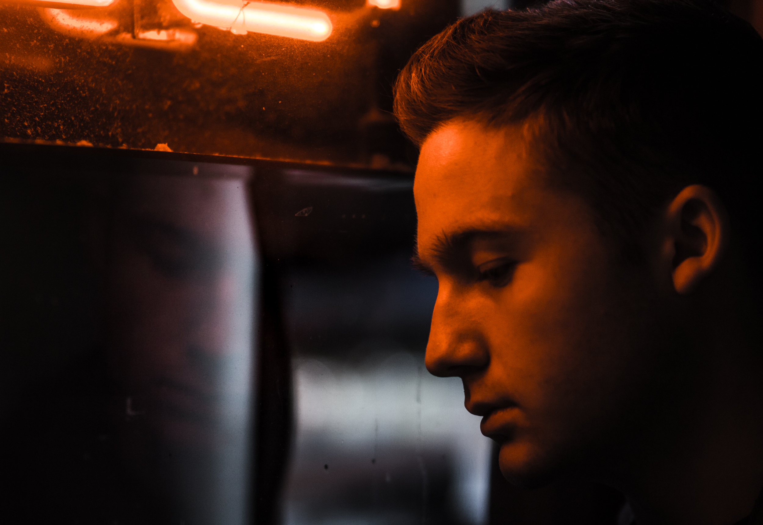 moody portrait of somber male looking up in front of orange neon sign, night
