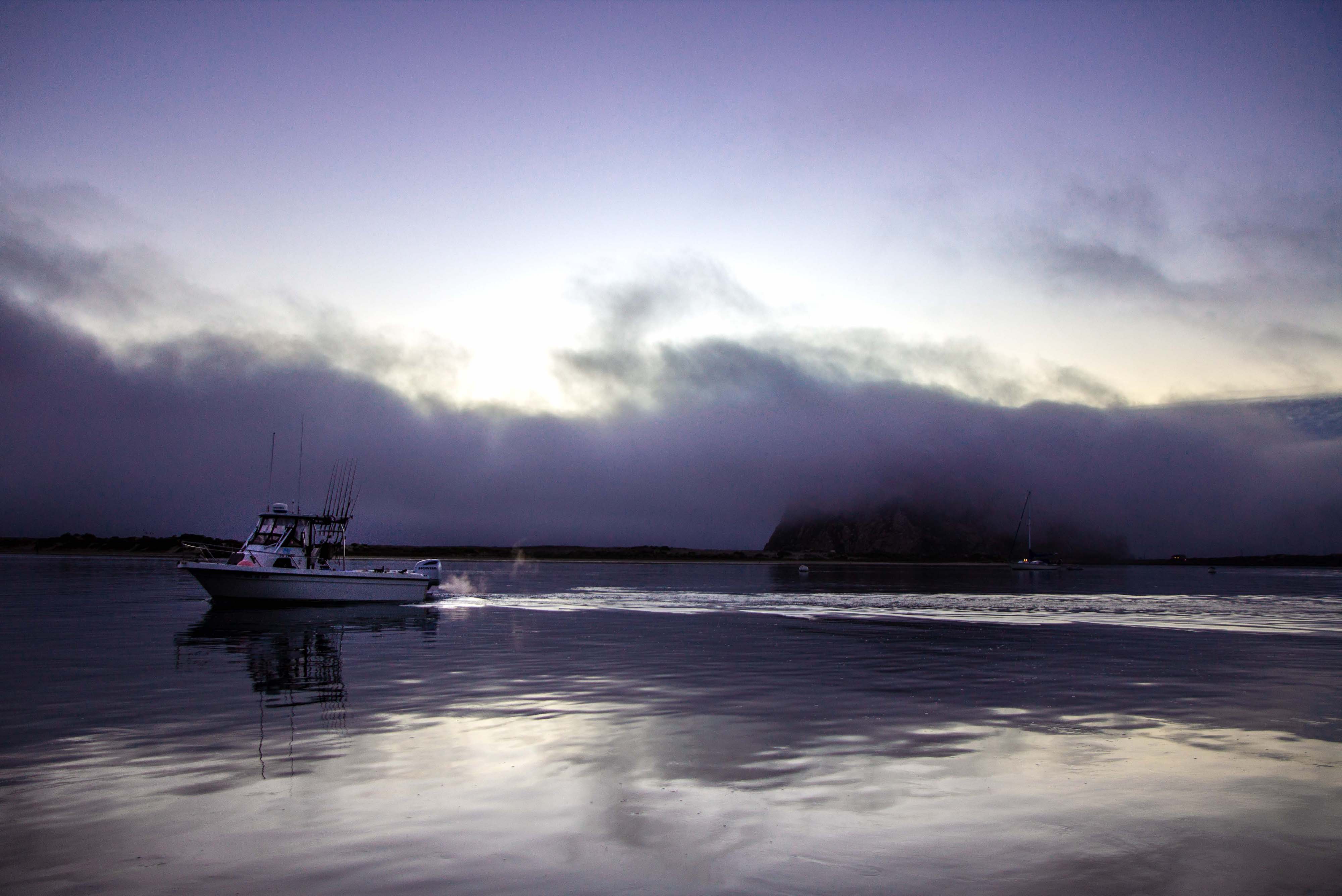 boat sailing in front of morro rock obscured by fog, morro bay california