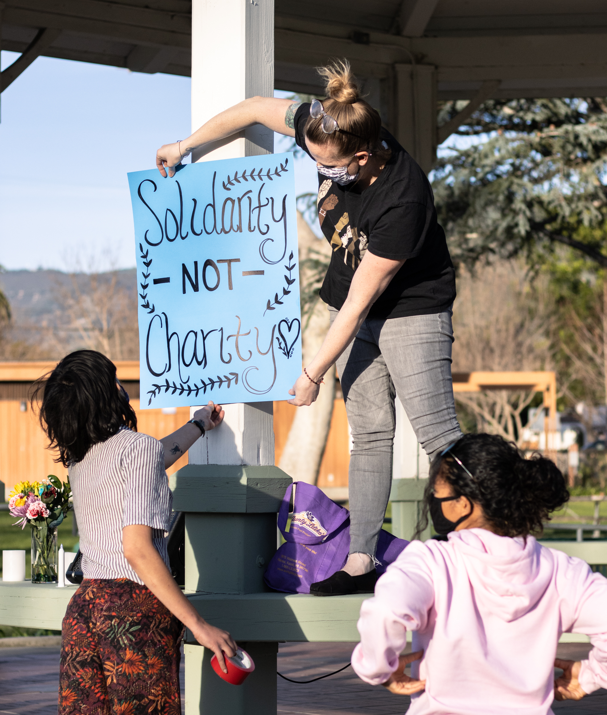 residents climbing the gazebo to align a sign which reads solidarity not charity