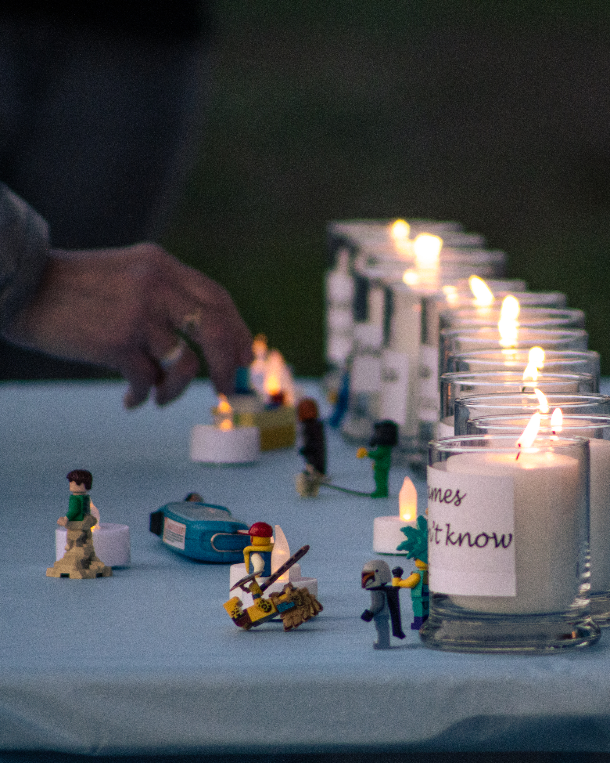 a hand places a lego figurine next to a row of candles