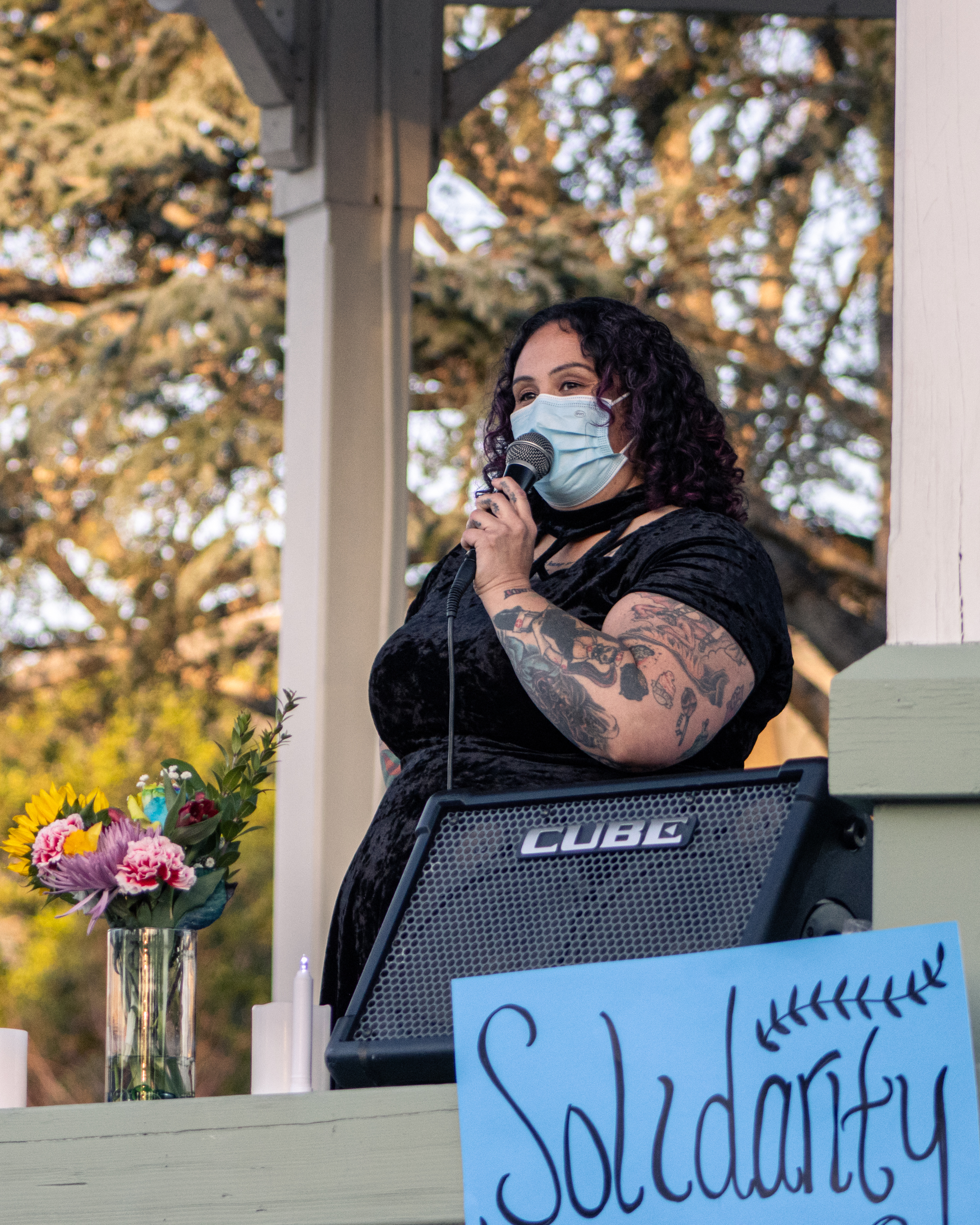 a woman gives a speech in front of a bouquet and a sign which reads solidarity