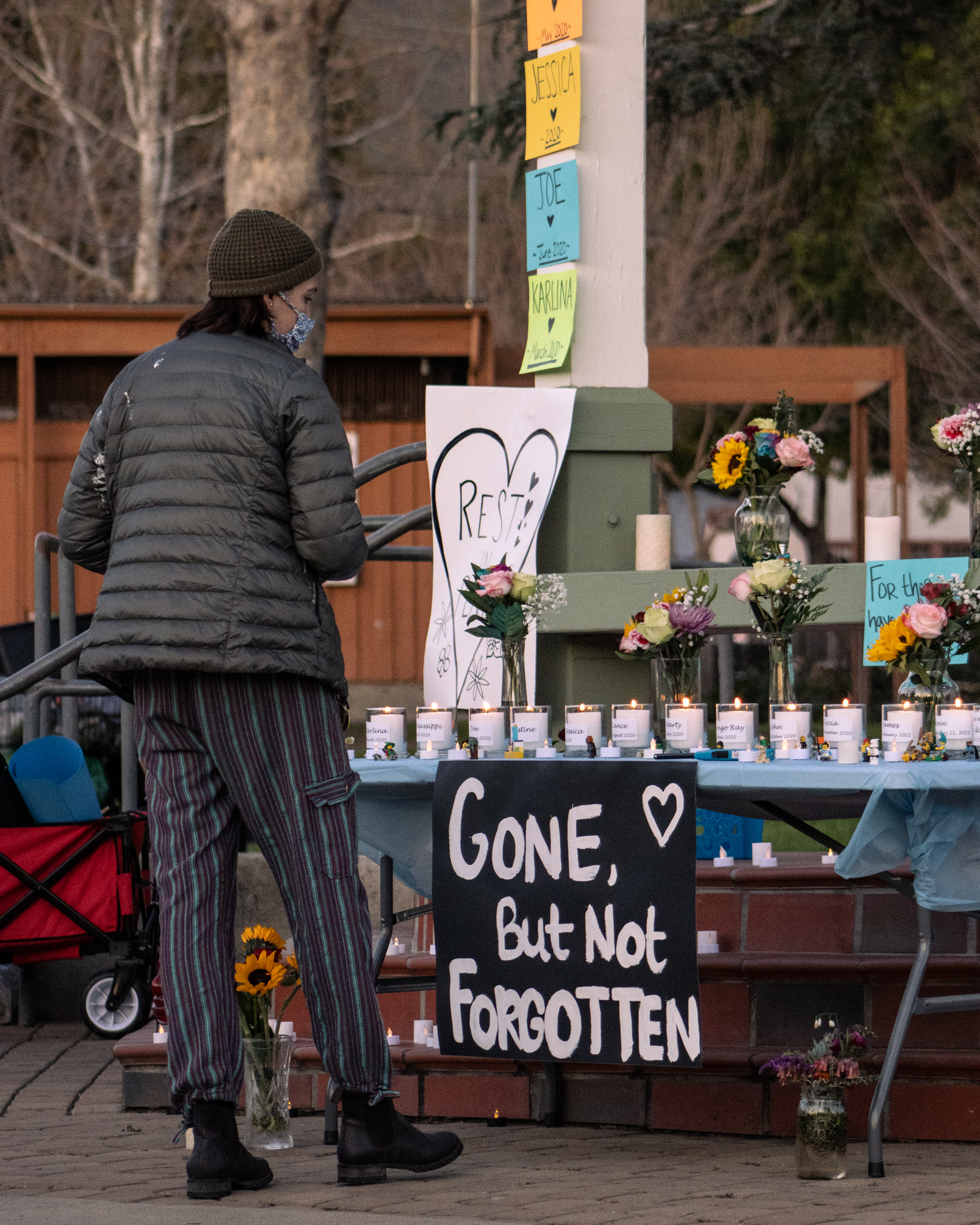 a community member observes a row of candles above a sign which reads gone but not forgotten