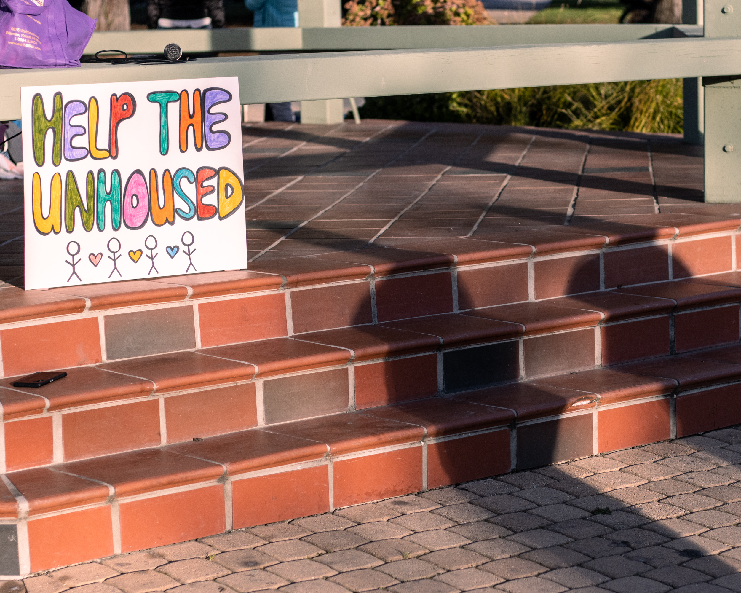 shadows cast on brick steps at sunset next to a sign which reads help the unhoused
