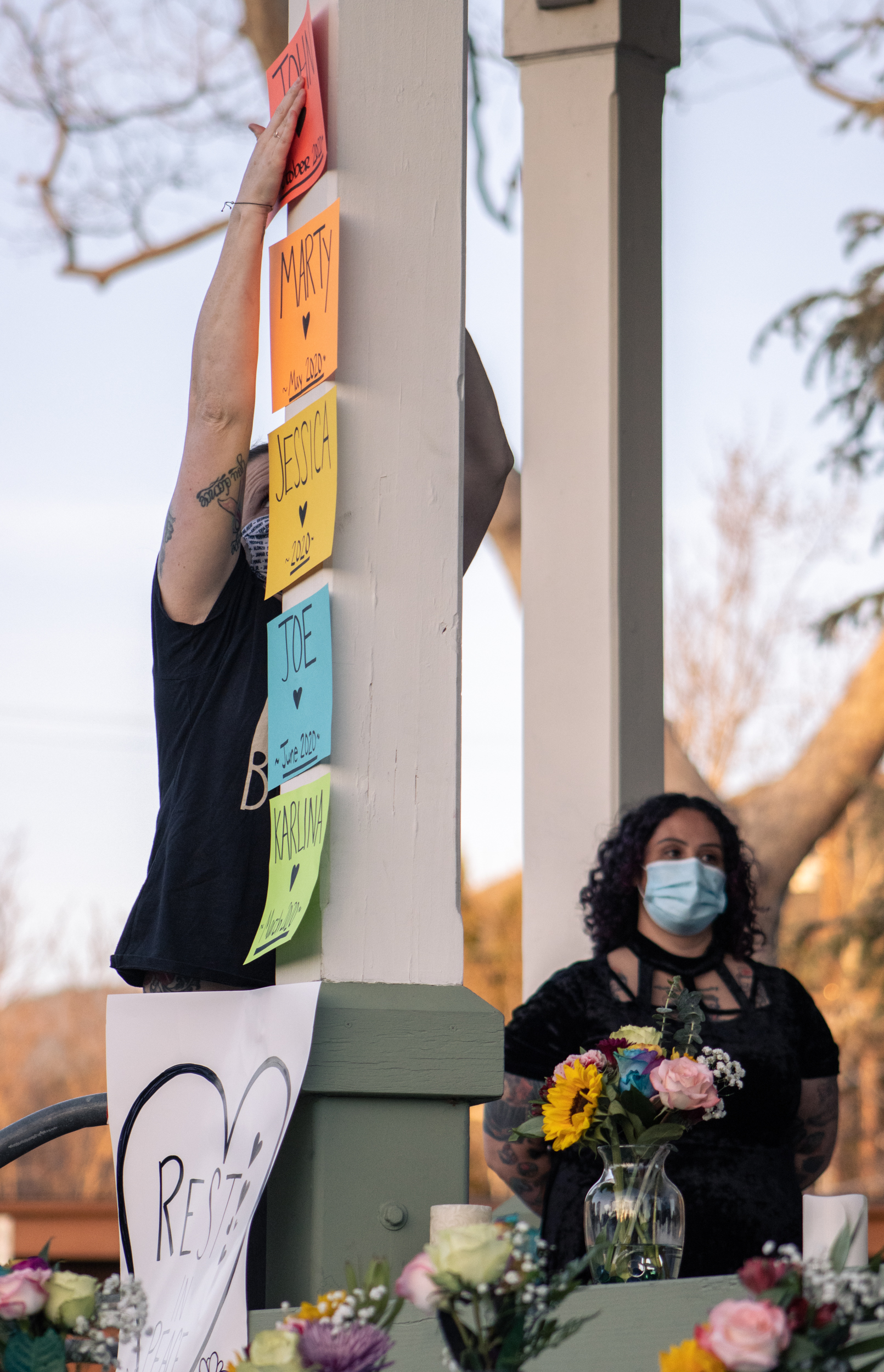 a community member strains herself to place a sign memorializing the name of a deceased neighbor on a white column, above several others