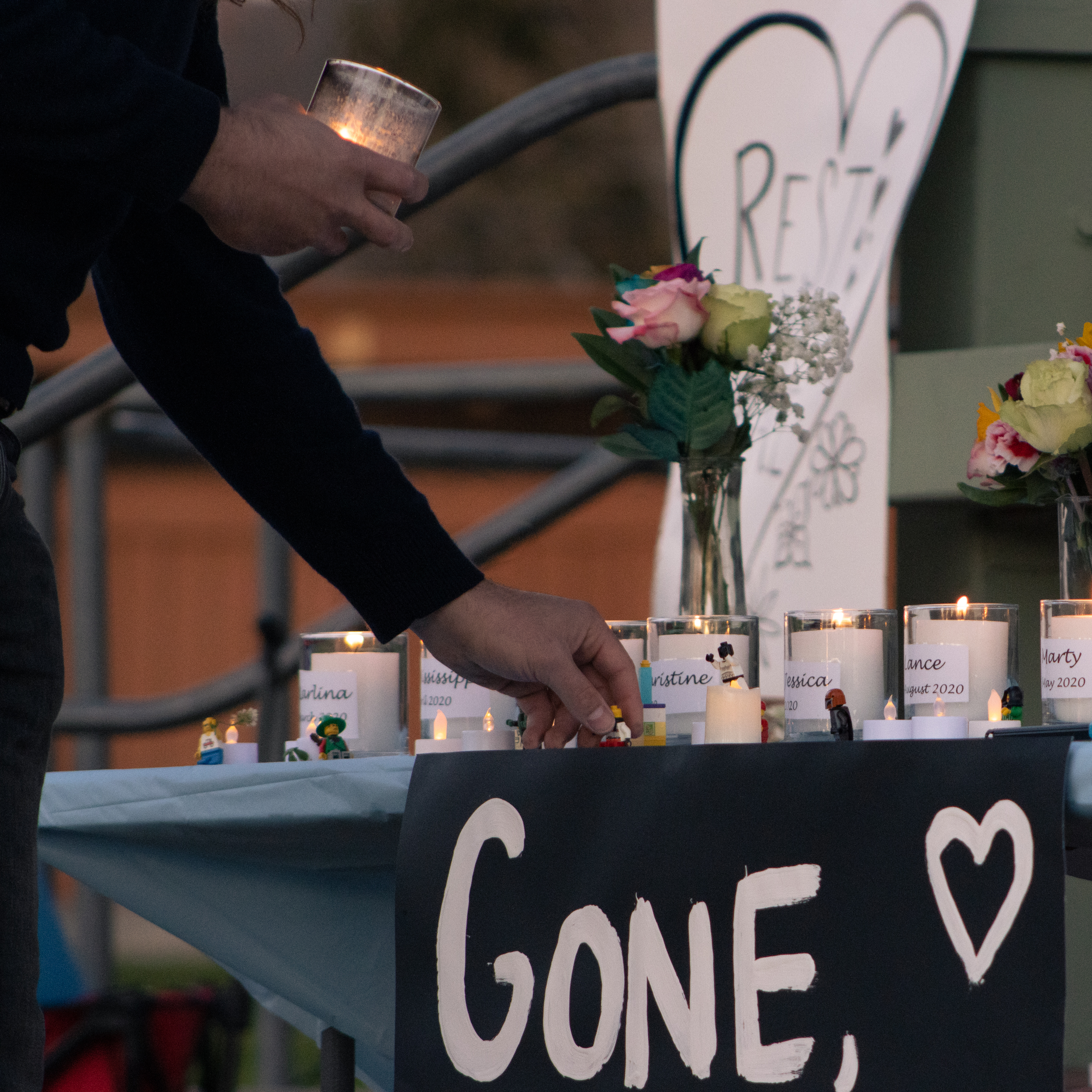 another hand holds a candle and leaves a lego figure on the table, above a sign which reads gone