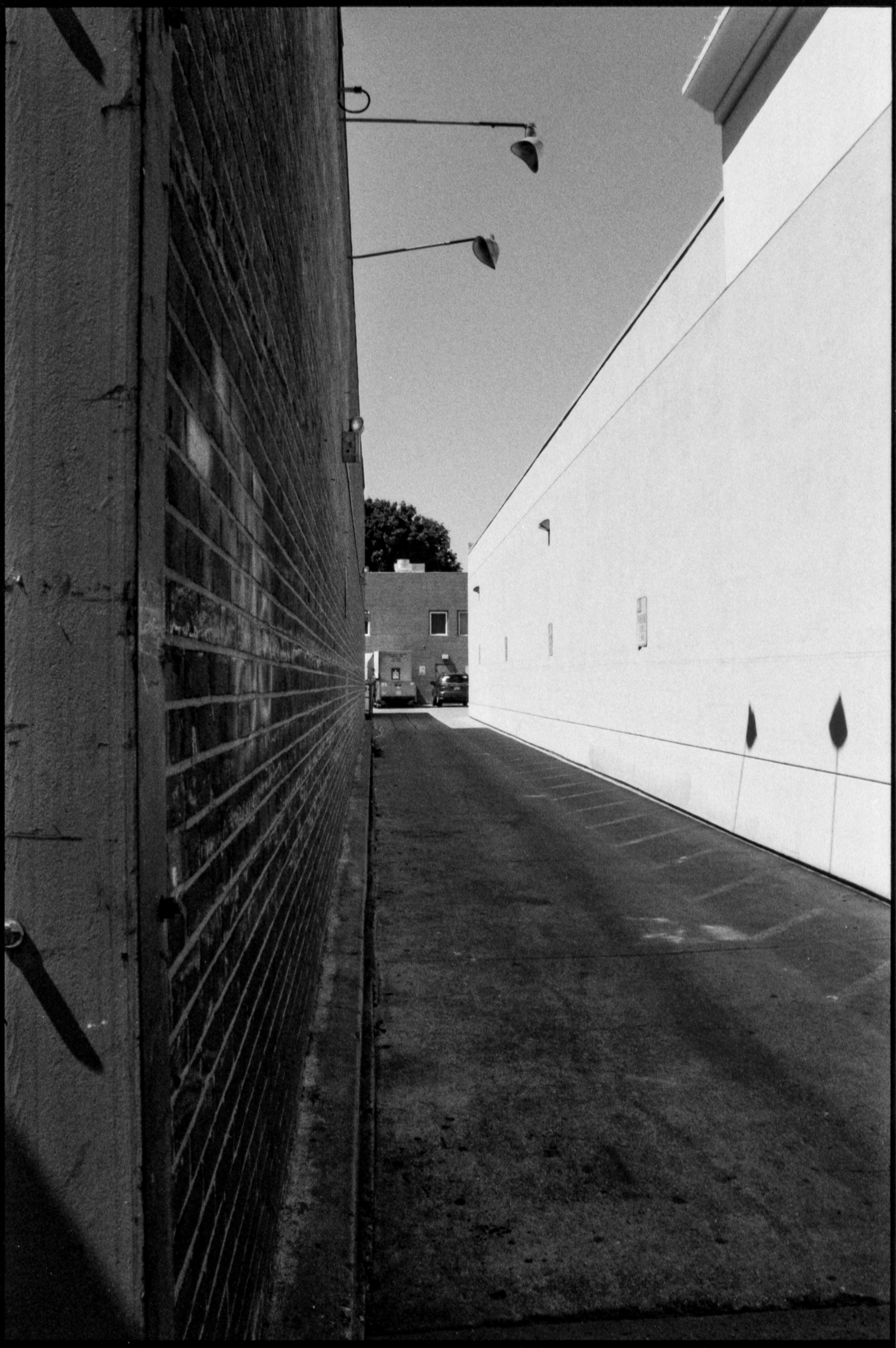a shaded back alley with overhead flood lights casting sharp shadows on the opposite wall