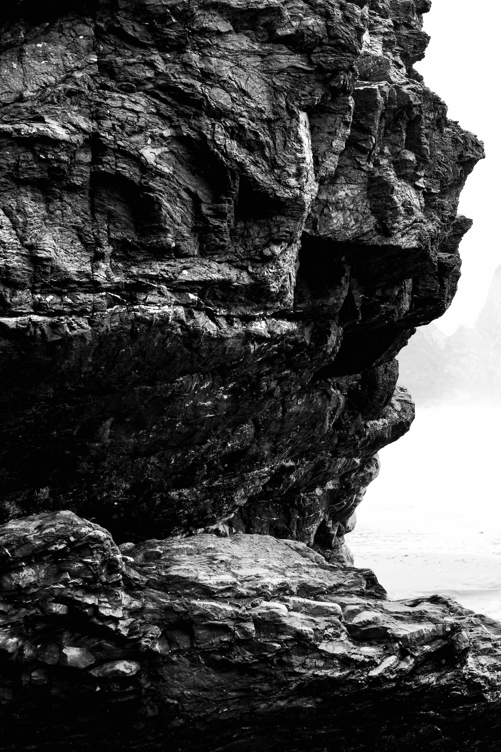 high contrast black and white photo of sharp faceted rock formations on a foggy beach