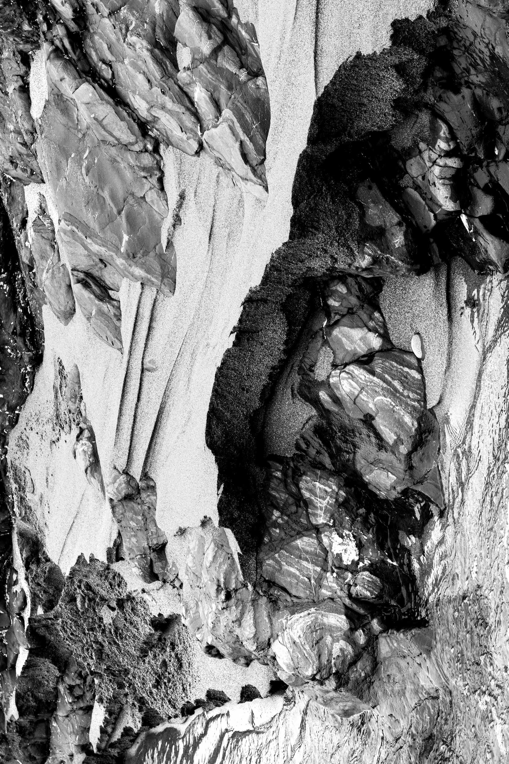 high contrast abstracted black and white photo of steep sand cliffs next to a beachside stream