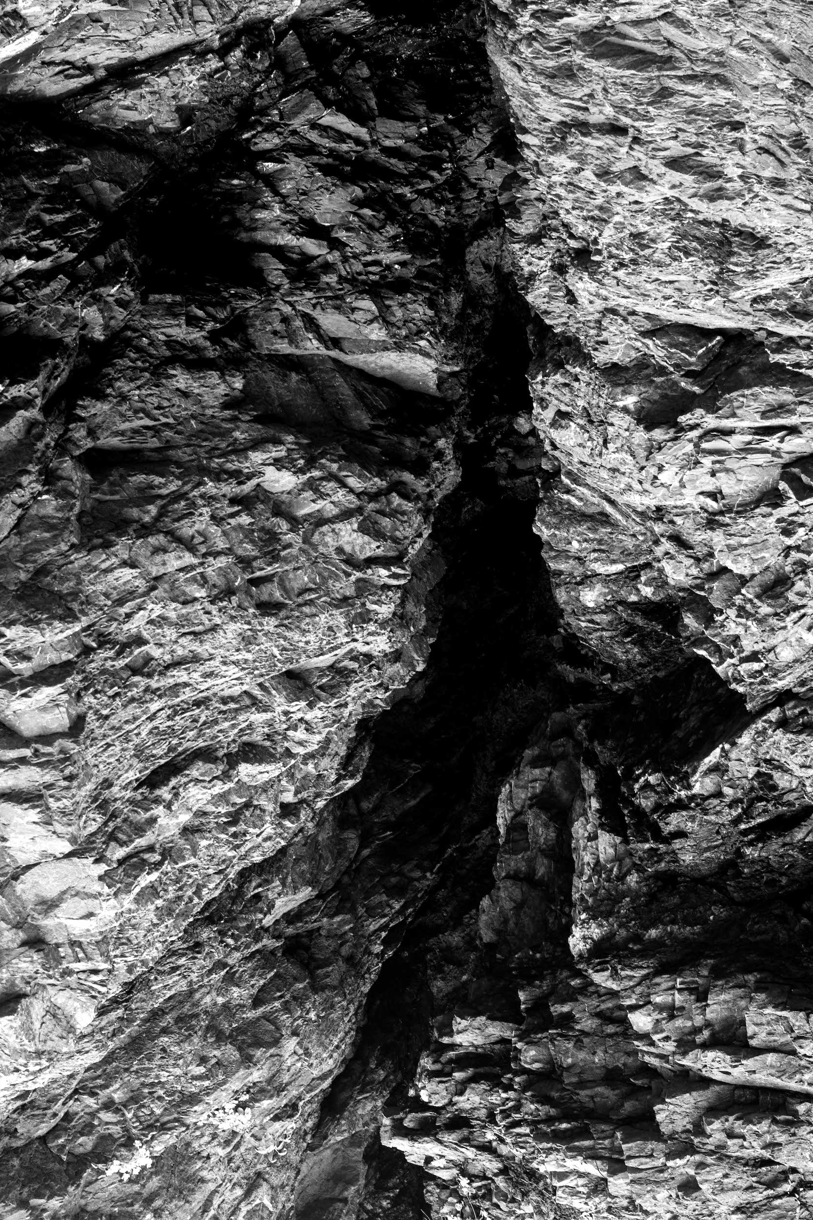 high contrast black and white photo of a sharp faceted rock formation with a dark crevice in the center