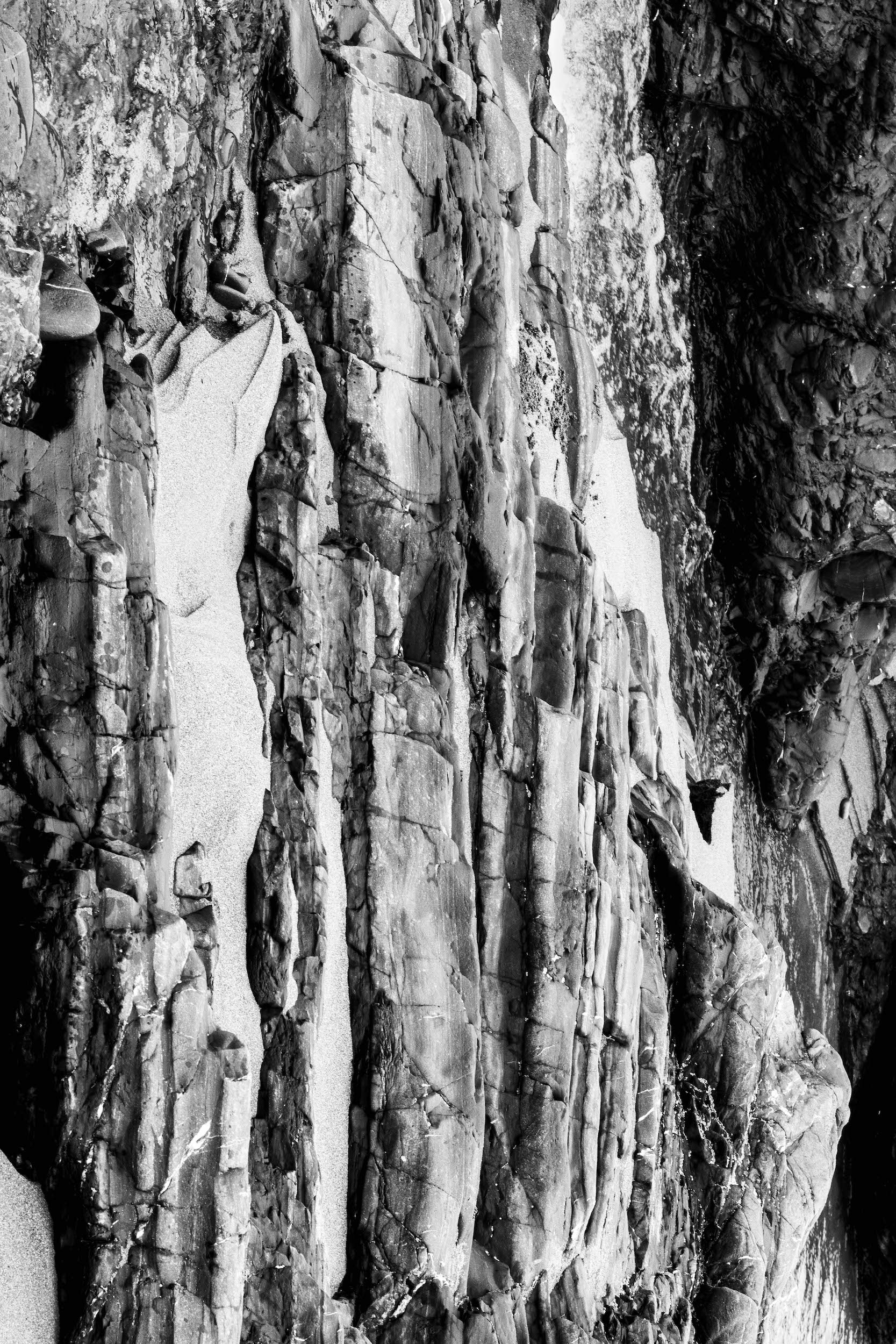 high contrast black and white photo of linear rock formations emerging from a sandy beach next to a stream
