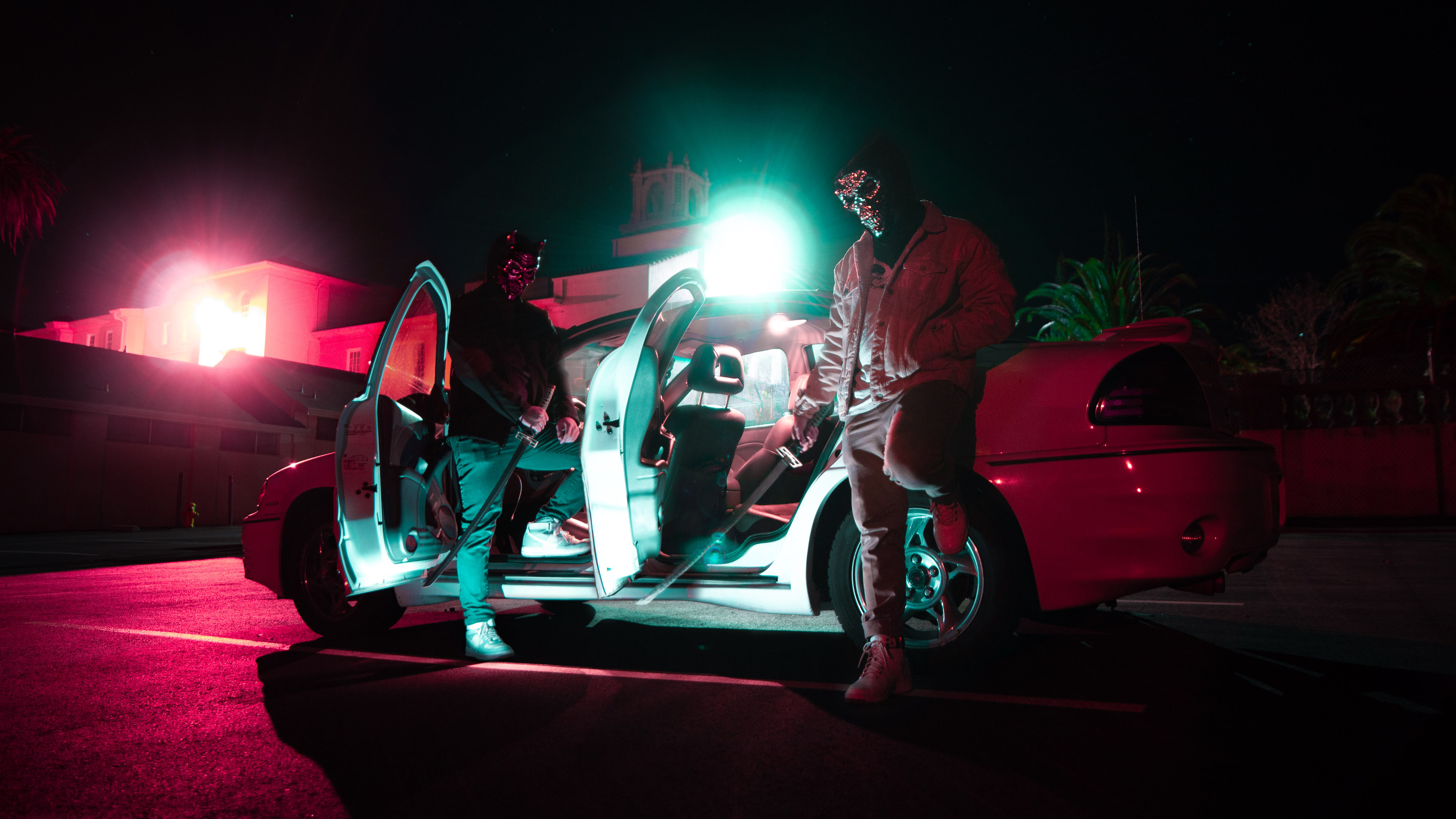 figures wearing skull and devil masks pose in front of open car at night, neon color scheme