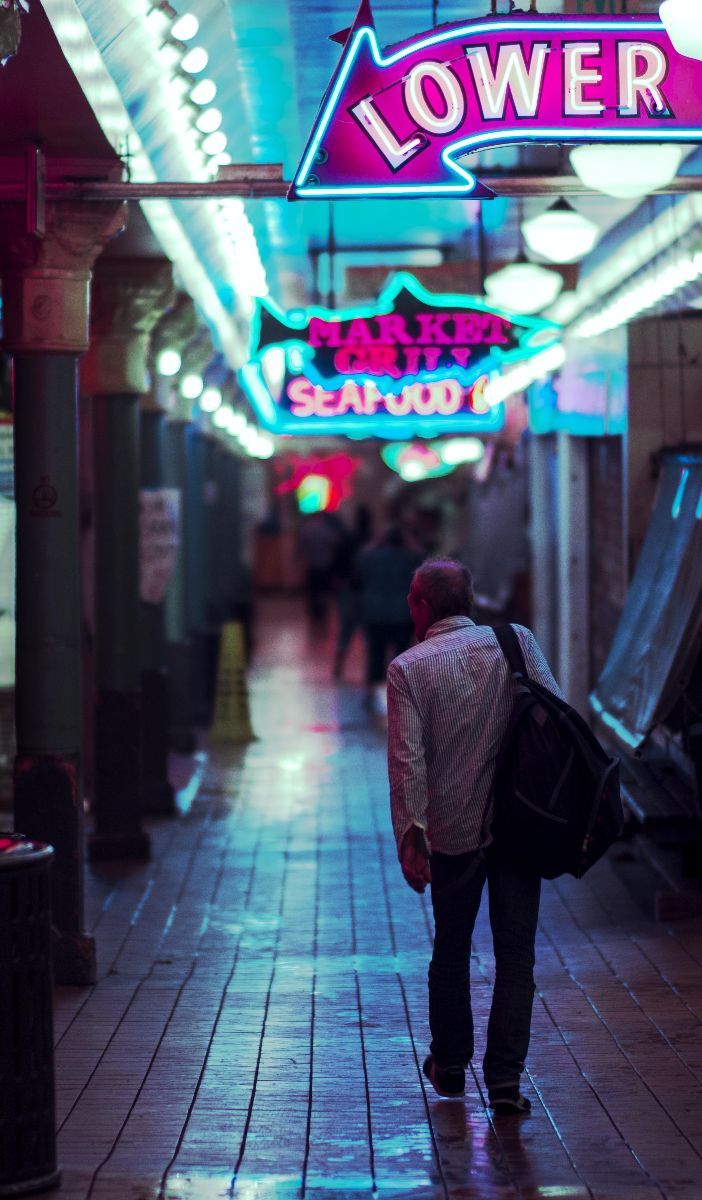 man walking under pike market neon lights at night